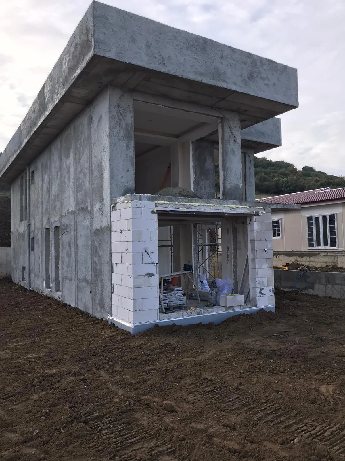 Betonarme yüzeyleri tamamlanmış iki katlı yapı ve saha görünümü